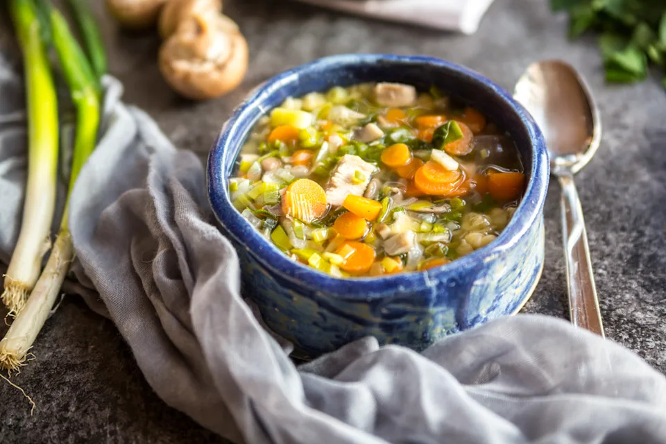 Overhead shot of a chicken and bean soup, with carrots and spring onions, in a blue bowl.