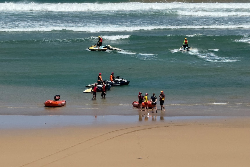 An image of a beach with search crews on orange inflatable boats and on jet skis on the water