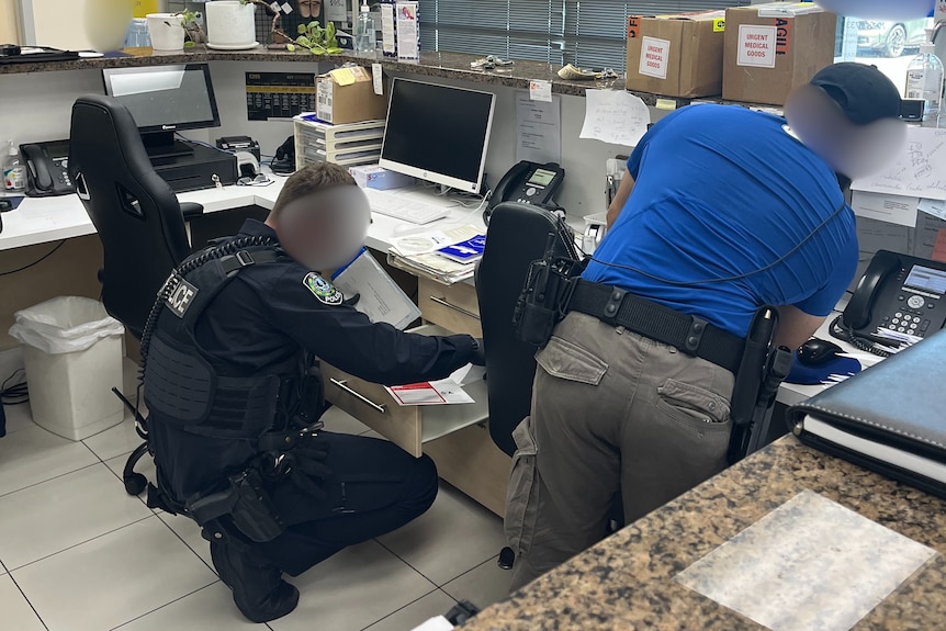Unidentifiable, male police officers rifling through desks in an office reception area.