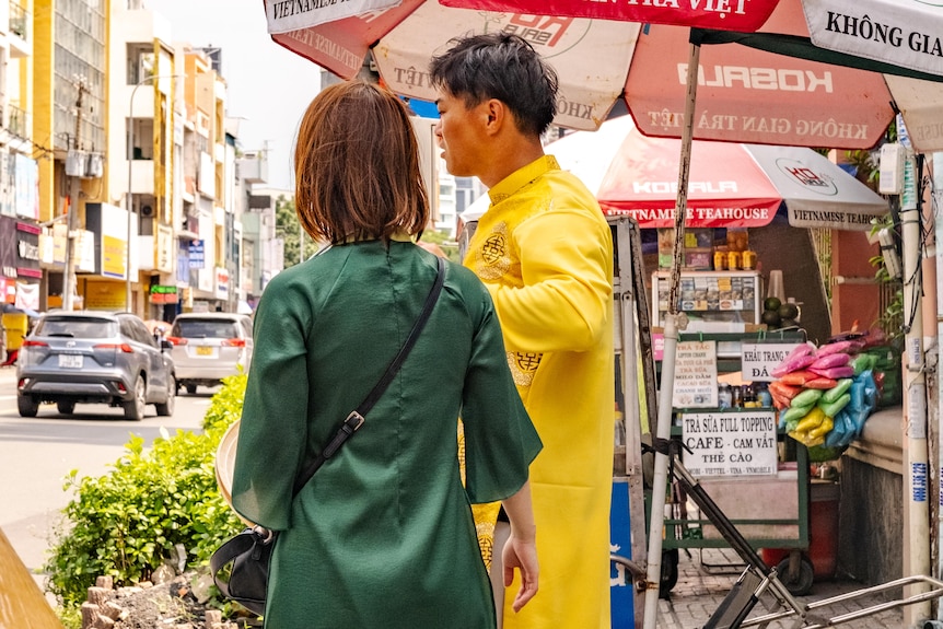 Two people in distinctive clothing stand on the roadside next to a small store.