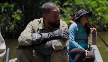 actor will smith in khakis seated with arms folded on is knees in a canoe rowing down a tropical river