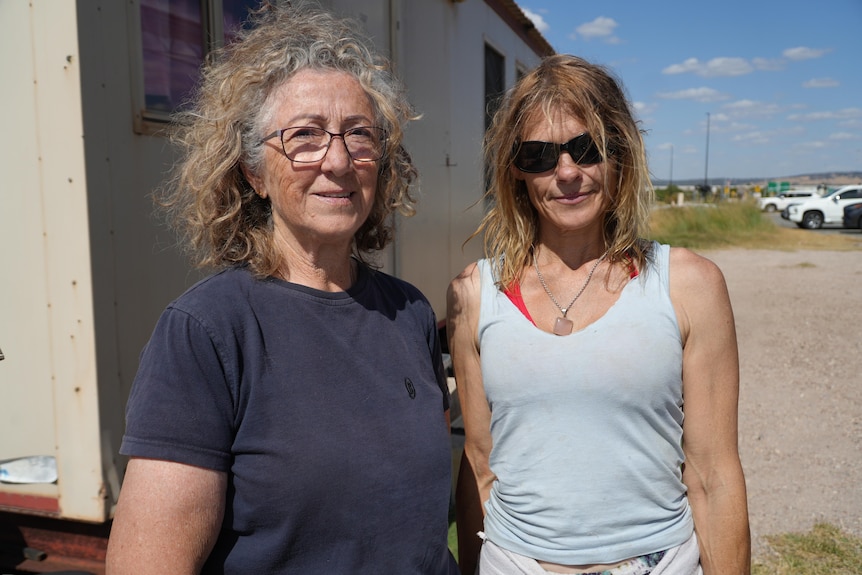 Two women stand in front of a shed. 
