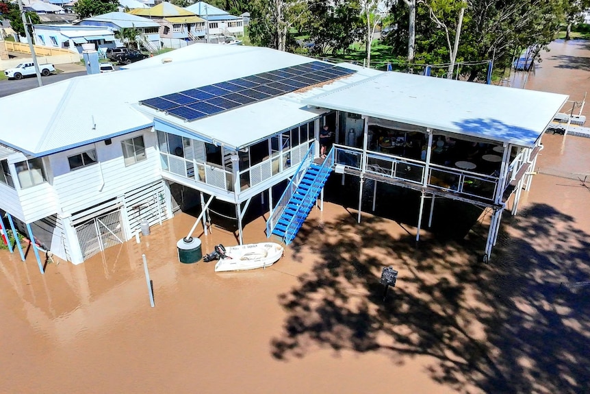 Drone shot of a brown river water around and underneath a house