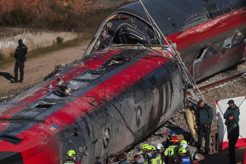 Two train carriages derailed and laying on their side along a track.
