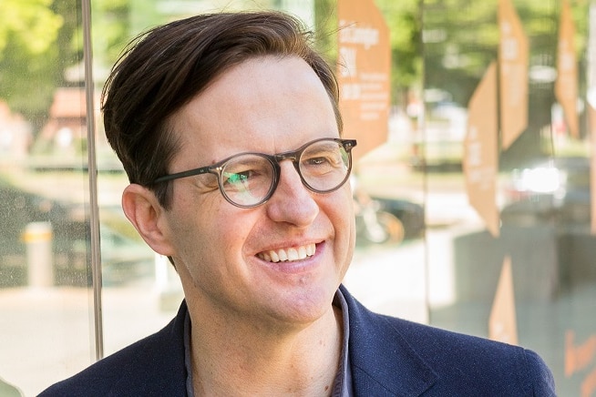 A portrait of a smiling man wearing glasses, looking off camera.
