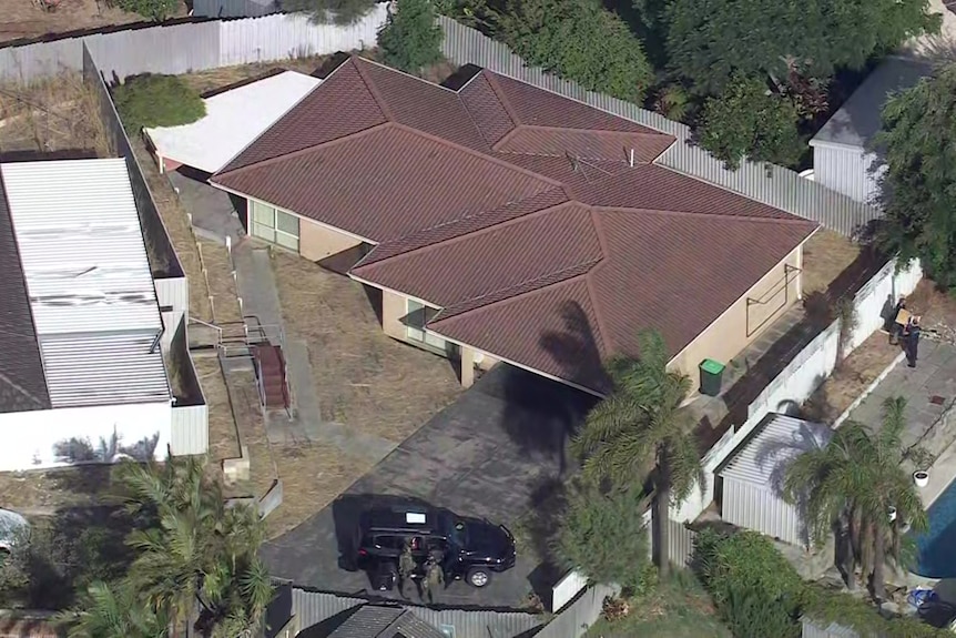 A police officer walks outside a home with cars alongside. 