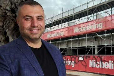 A man smiles, with a building site with a Nicheliving banner in the background.