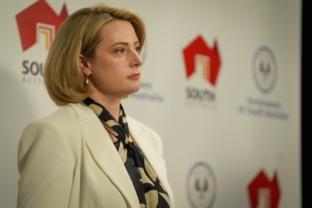 A side on photo of a woman with a serious expression standing in front of an SA government sign