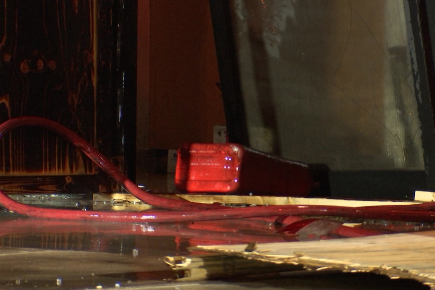 A red container lies on its side beside red fire hoses and a broken glass panel at night.