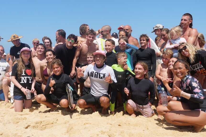 Josh sitting in front of a crowd of people throwing a shaka with his hands. 