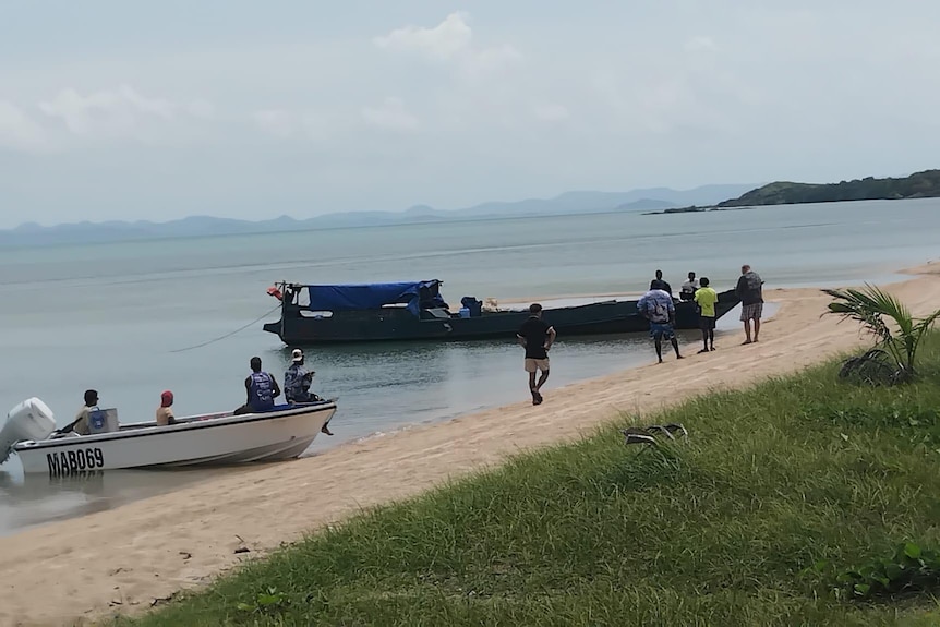 several small fishing boats and people on a tropical island beach.