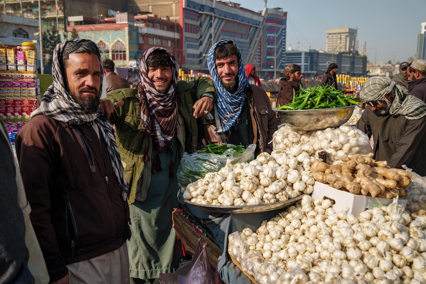 Three men smile next to a stand displaying garlic in Kabul.
