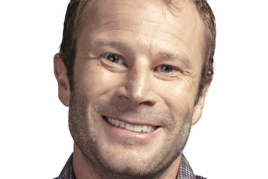 A man smiles at the camera with head tilted wearing a striped shirt