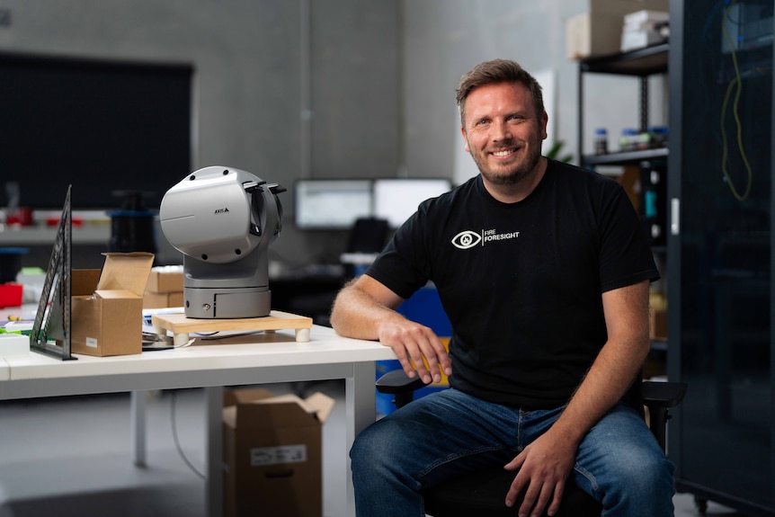 Man smiles for photo, sitting at a desk