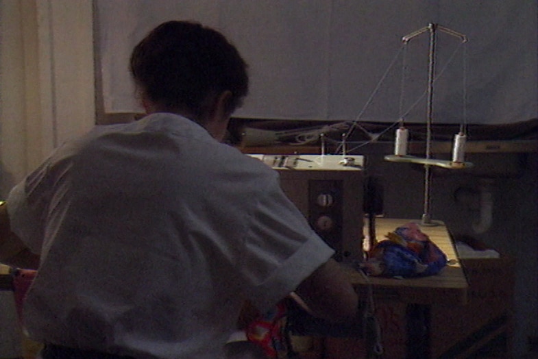 A woman on a sewing machine photographed from behind. 