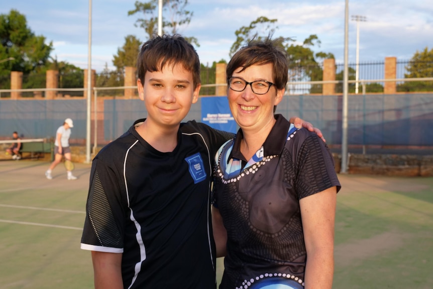 a teenage boy and his mum smiling, standing on a tennis club