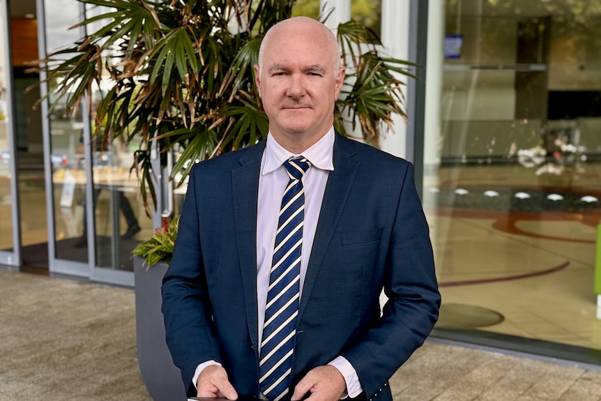 a man in a suit looks serious while holding a pile of papers