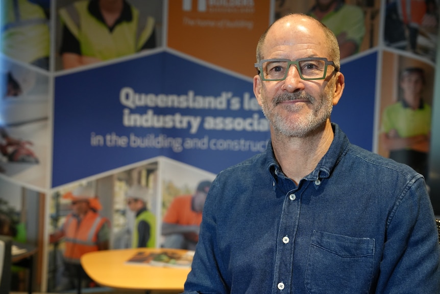 a man with glasses and a blue shirt smiles at the camera