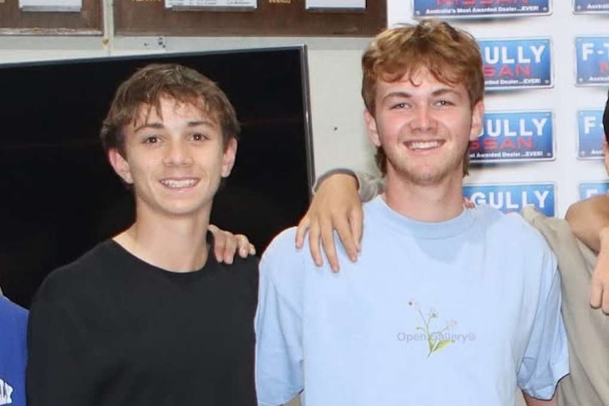 Two teenage boys stand next to each orther smiling.
