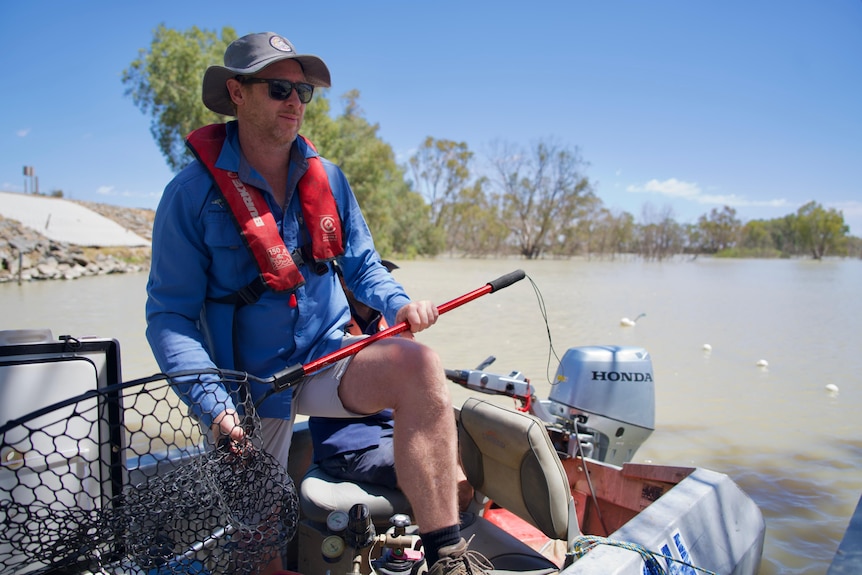 A man from NSW DPIRD Fisheries holds a fishing net at Lake Wetherell Menindee