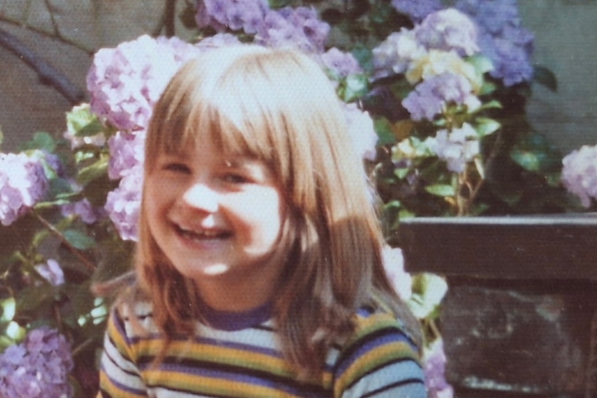 An old photo of a young girl with brown hair and a fringe smiling.