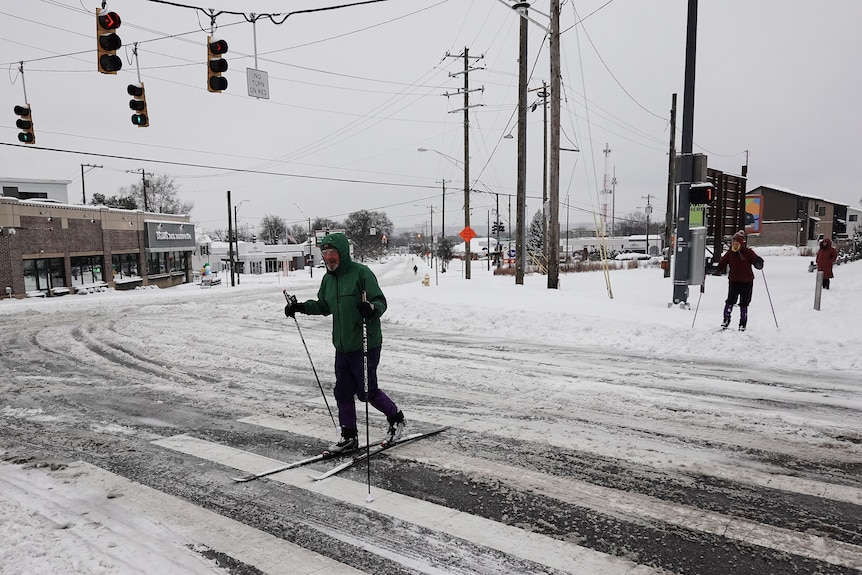 A man crossing a zebra crossing on skis.