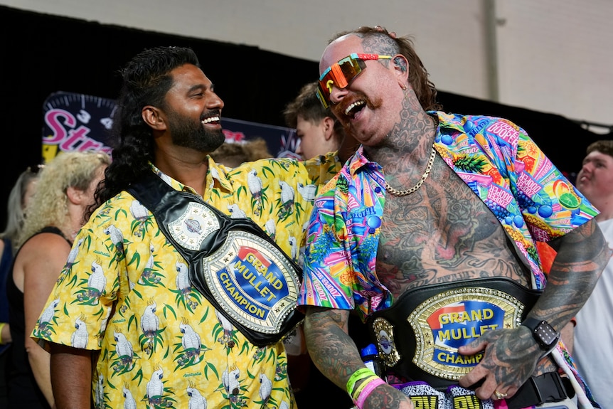 Two men with mullets and awards congratulate each other.