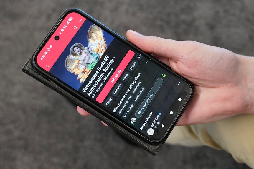 A man holding a phone with a Vietnamese Banh Mi Appreciation Society Facebook group open on the phone.