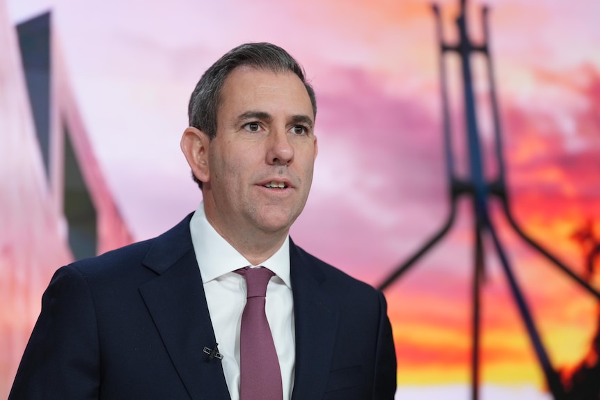 A man in a suit and tie stands in front of a sunset