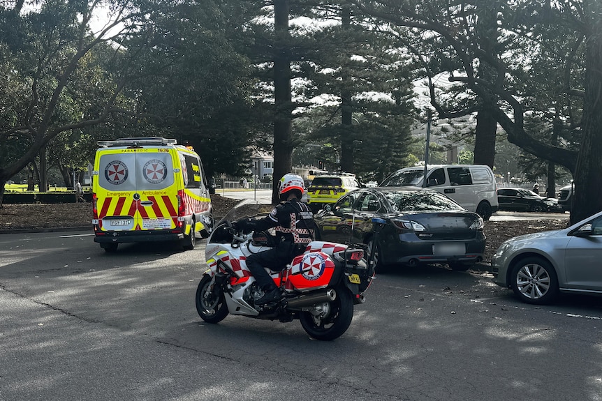 an ambulance followed by a police officer on a motorbike