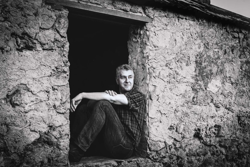Ockert Le Roux sits in an open frame of a stone wall smiling, looking out.
