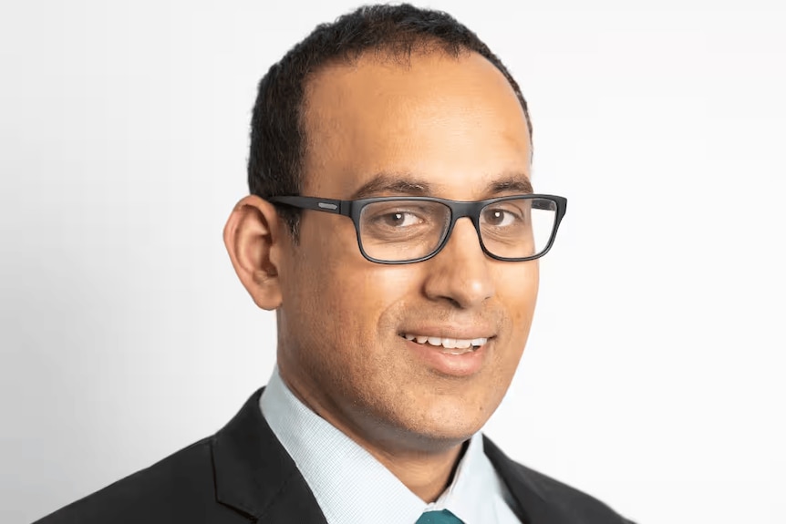 A head shot of a man in black glasses and suit.
