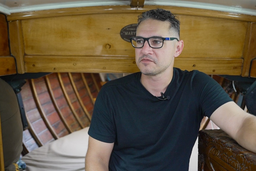 A man wearing a black tshirt and glasses sitting inside a boat