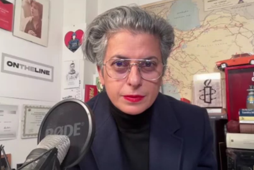 A woman wearing glasses sits at a microphone.