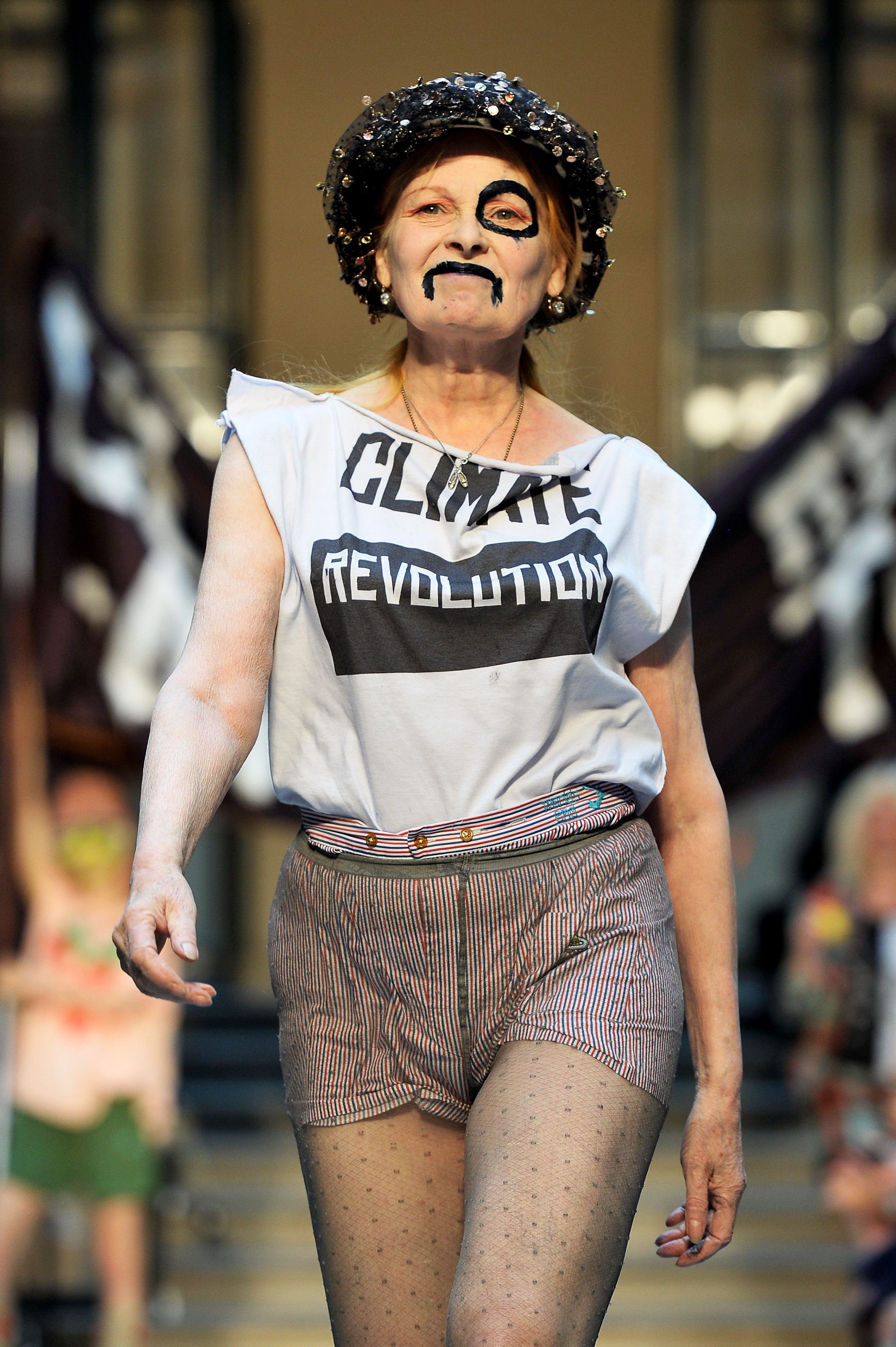 Vivienne Westwood walks the runway in tweed shorts and a tshirt that says climate revolution