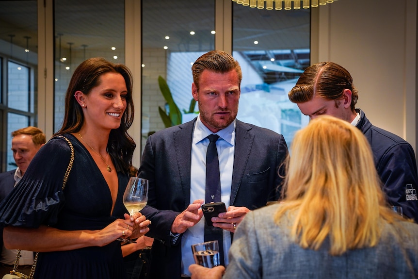 A man and woman in formal attire chat to people at an event.