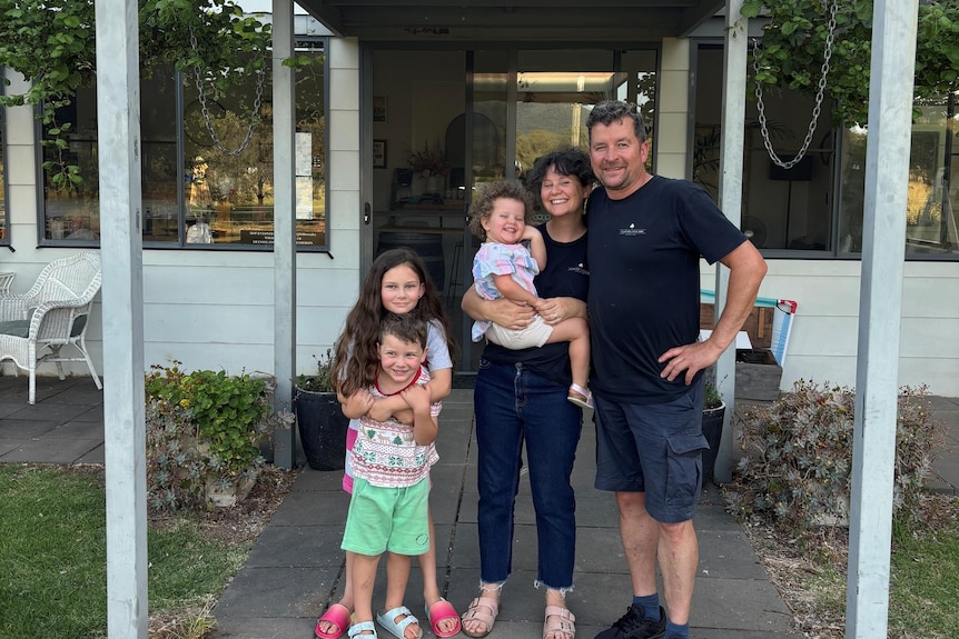 A man and a woman with three young children stand outside a house.