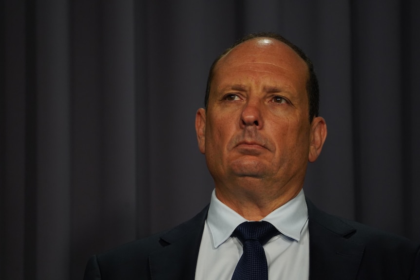 A close up shot of a man's face, looking off-camera, wearing suit and tie