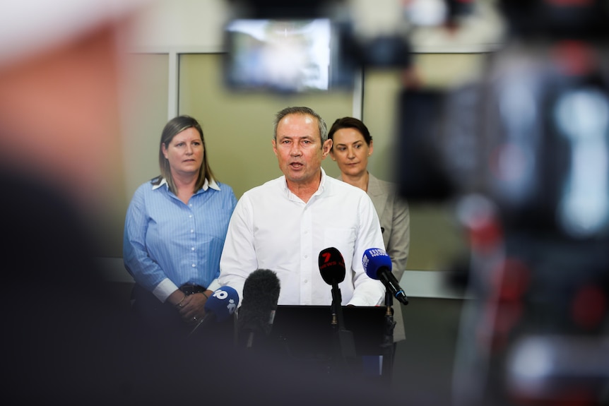 A man stands with two women behind a lecturn