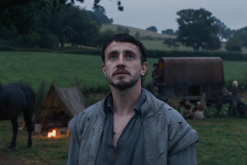 A man stands in a field in front of a horse and cart