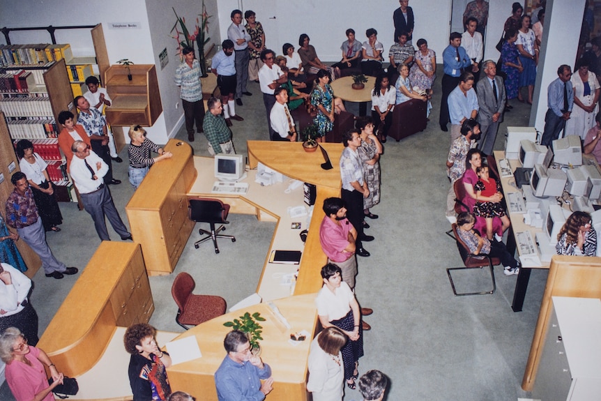 A room with desk's, computers, full of people.