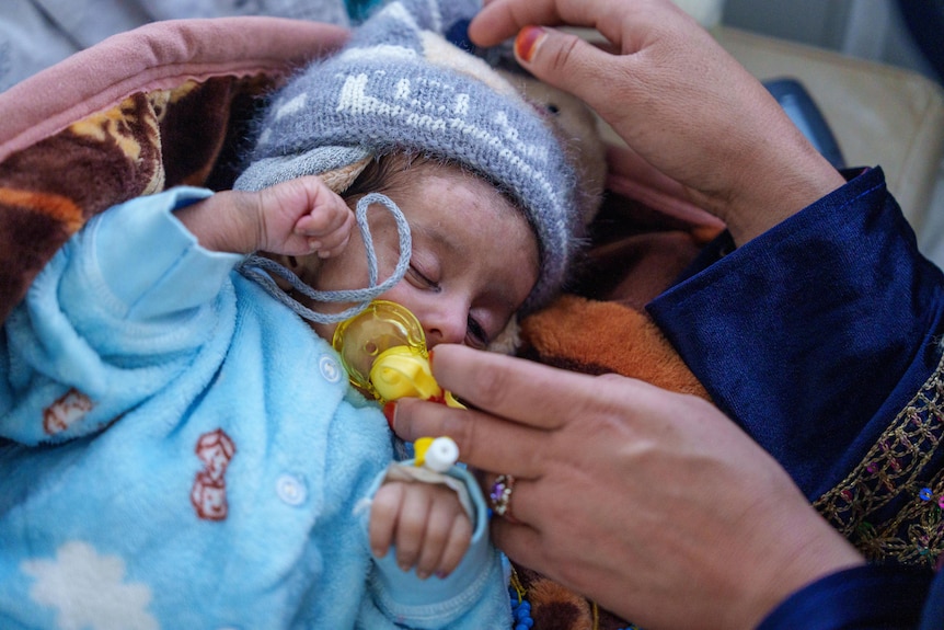 A mother settles a blanket around her sleeping baby in an Afghanistan hospital.