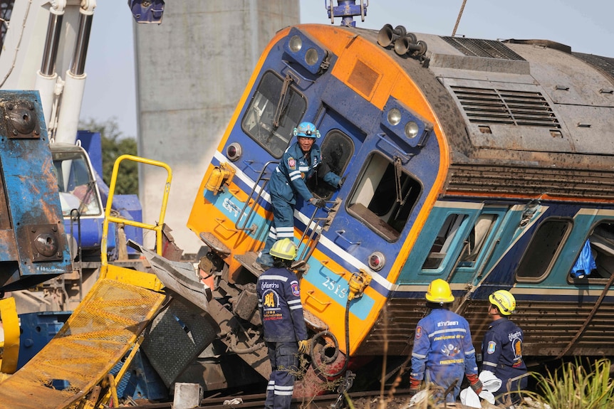 A rescue teams stand near a damaged train with a crane in the background
