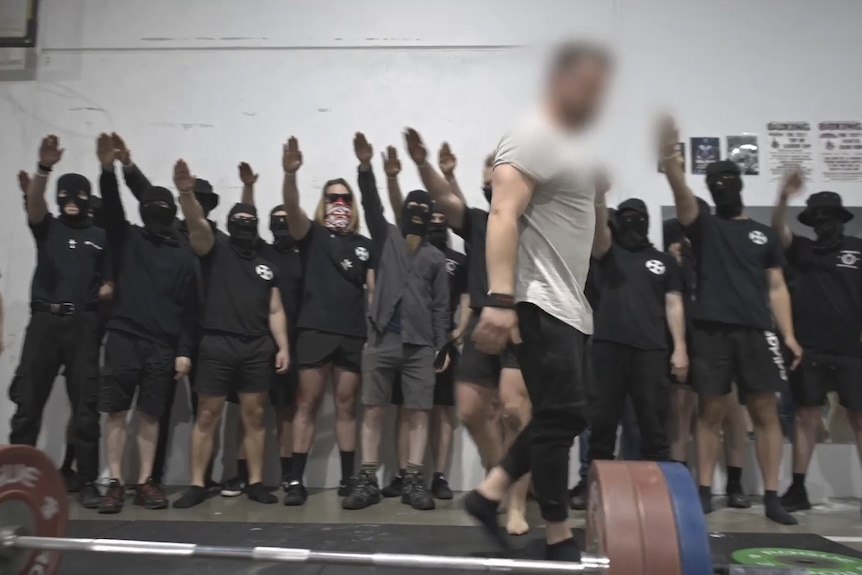 A group of men stand in a group with most holding up their right arm in an apparent Nazi salute.
