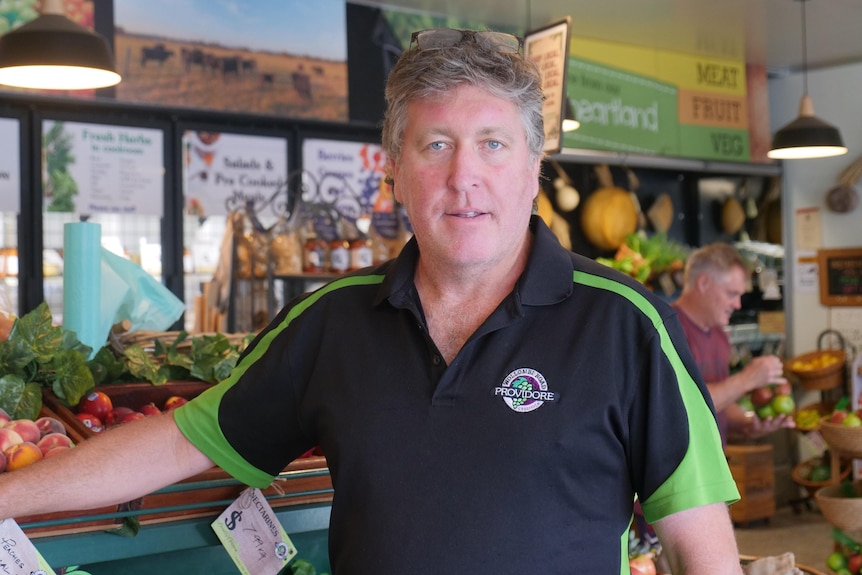 A man stands in front of a stand of fruit and vegetables. 