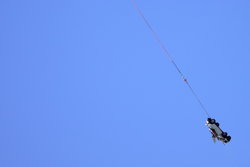A car being winched from the sea by a helicopter along the Great Ocean Road.