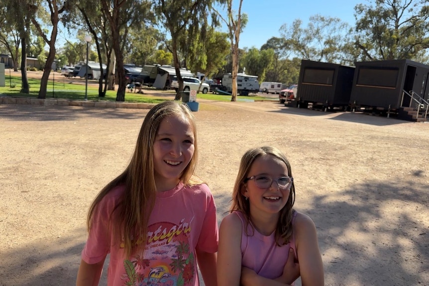 Two young girls smiling in front of a caravan park.