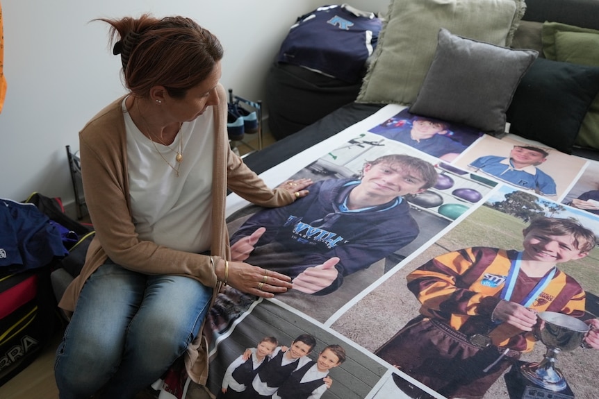A woman sits on a bed. The bedspread is covered in images of her son.