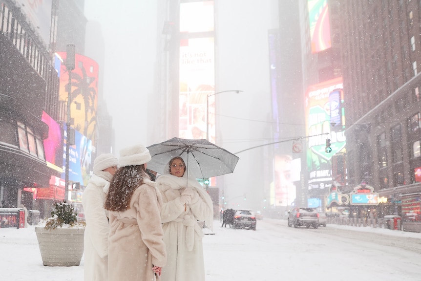 Women wearing white fur coats and hats in a snowy Times Square, New York.