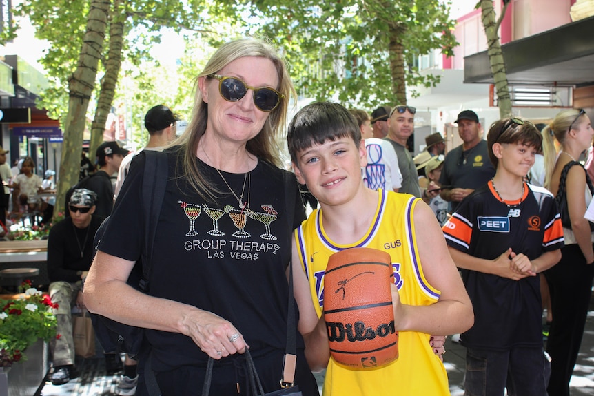 A boy holding a signed basketball stands next to his mum.